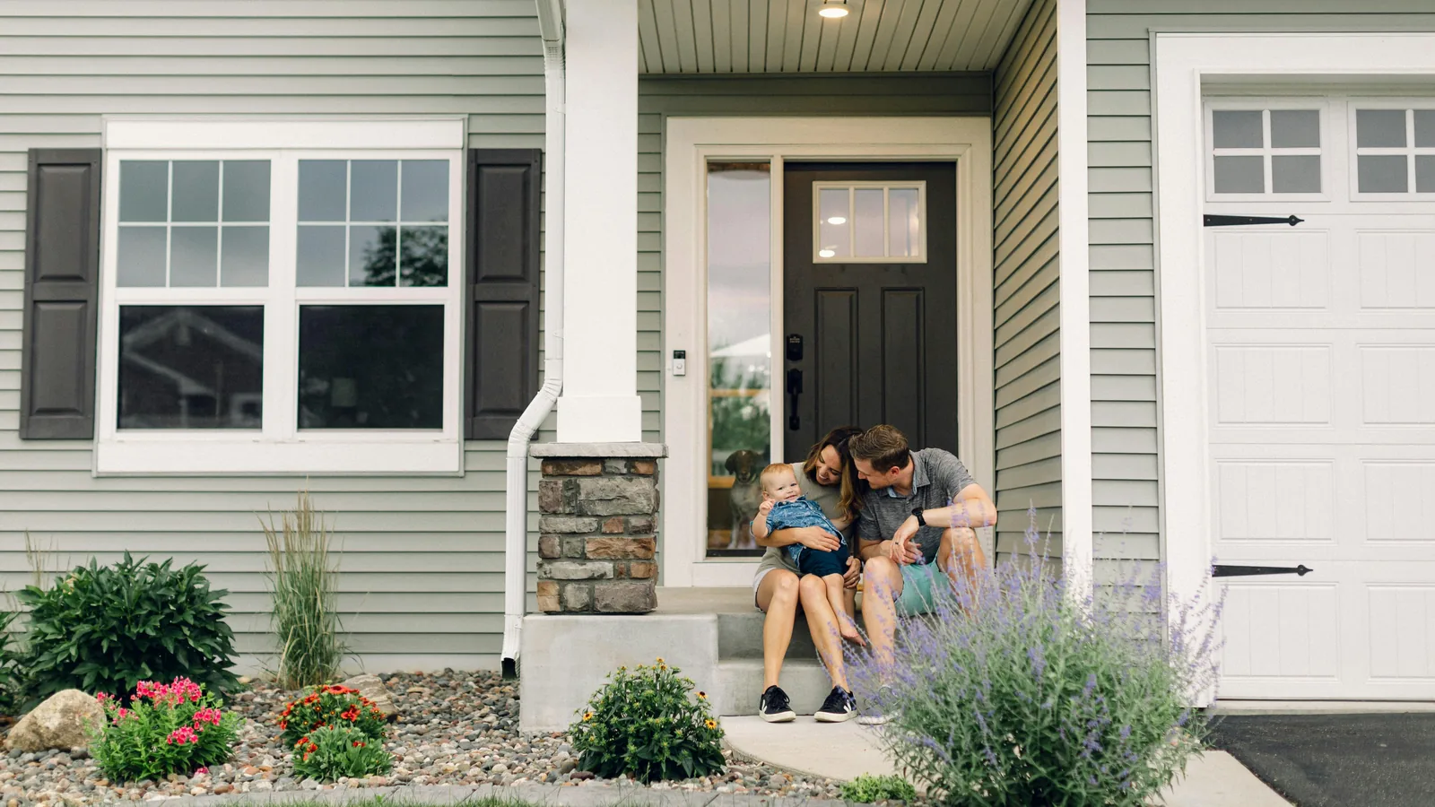 A young couple with a baby, sitting on the front steps of a house.